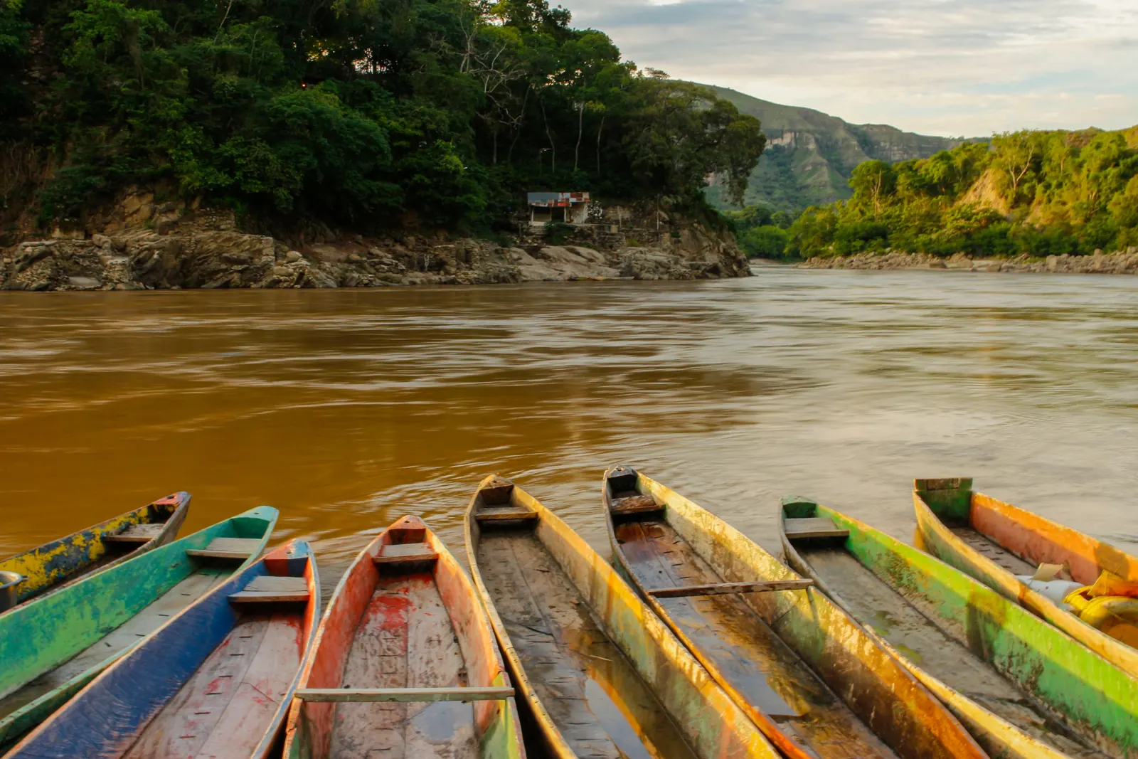 Canoas de madera pintadas a la orilla de un río caudaloso entre montañas verdes