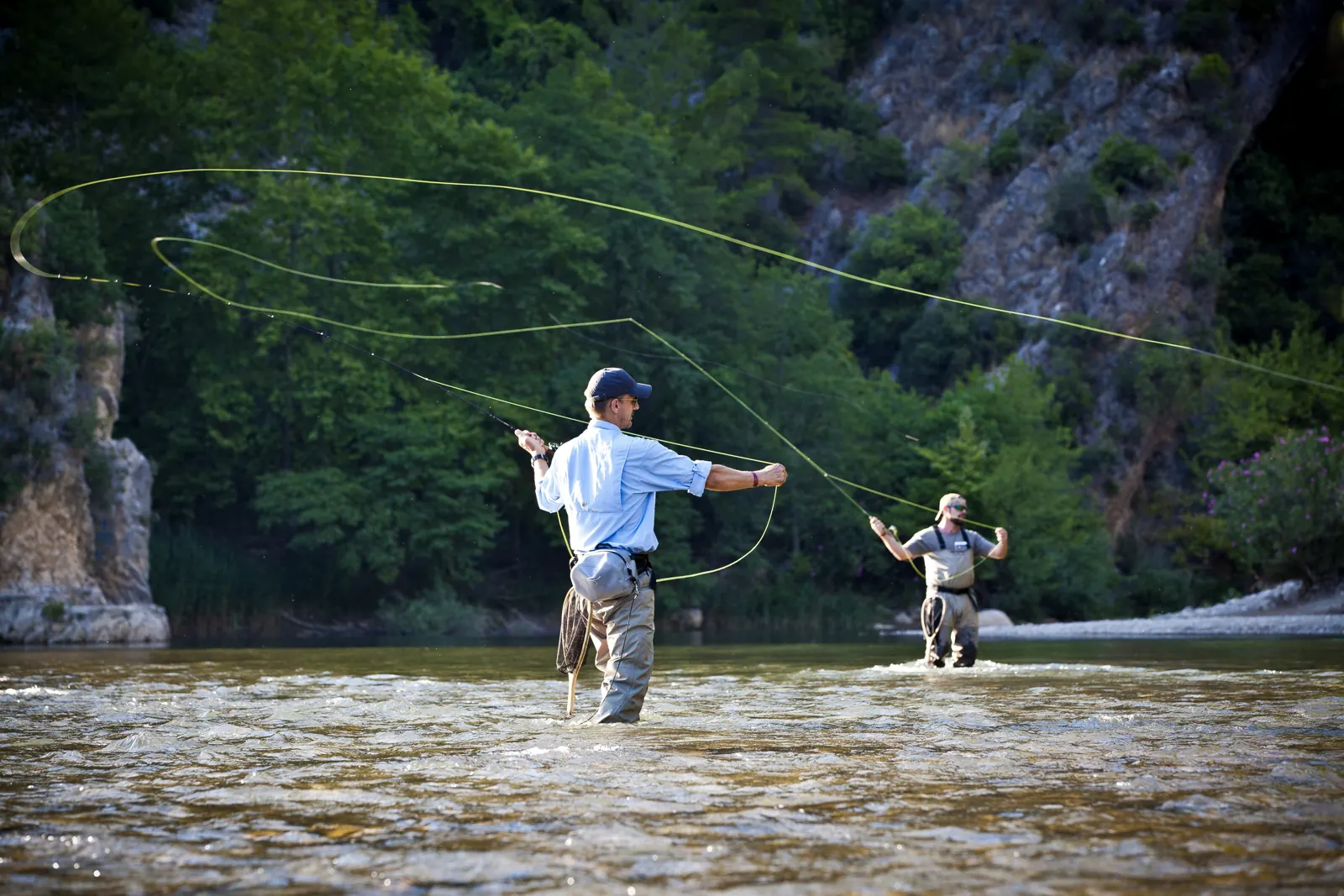Dos pescadores lanzando con caña de mosca dentro de un río de montaña