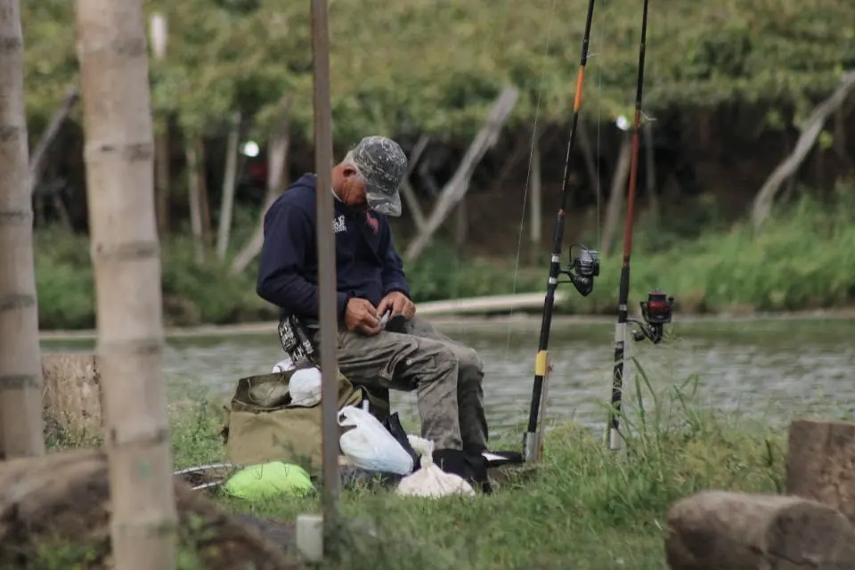 Pescador preparando su equipo a la orilla del río, con dos cañas y carretes listos
